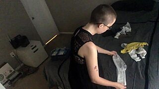 Bald girl starts folding laundry with KonMari method in clothed setting. She ignores voyeur while staying nude and hairless.